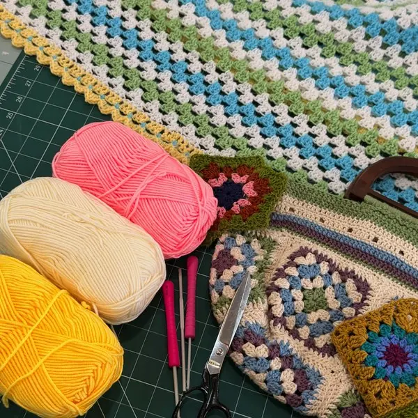 Granny-square crochet blanket and bag with balls of yarn and hooks